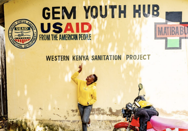 A woman pointing at a sign of the USAID Western Kenya Sanitation Project